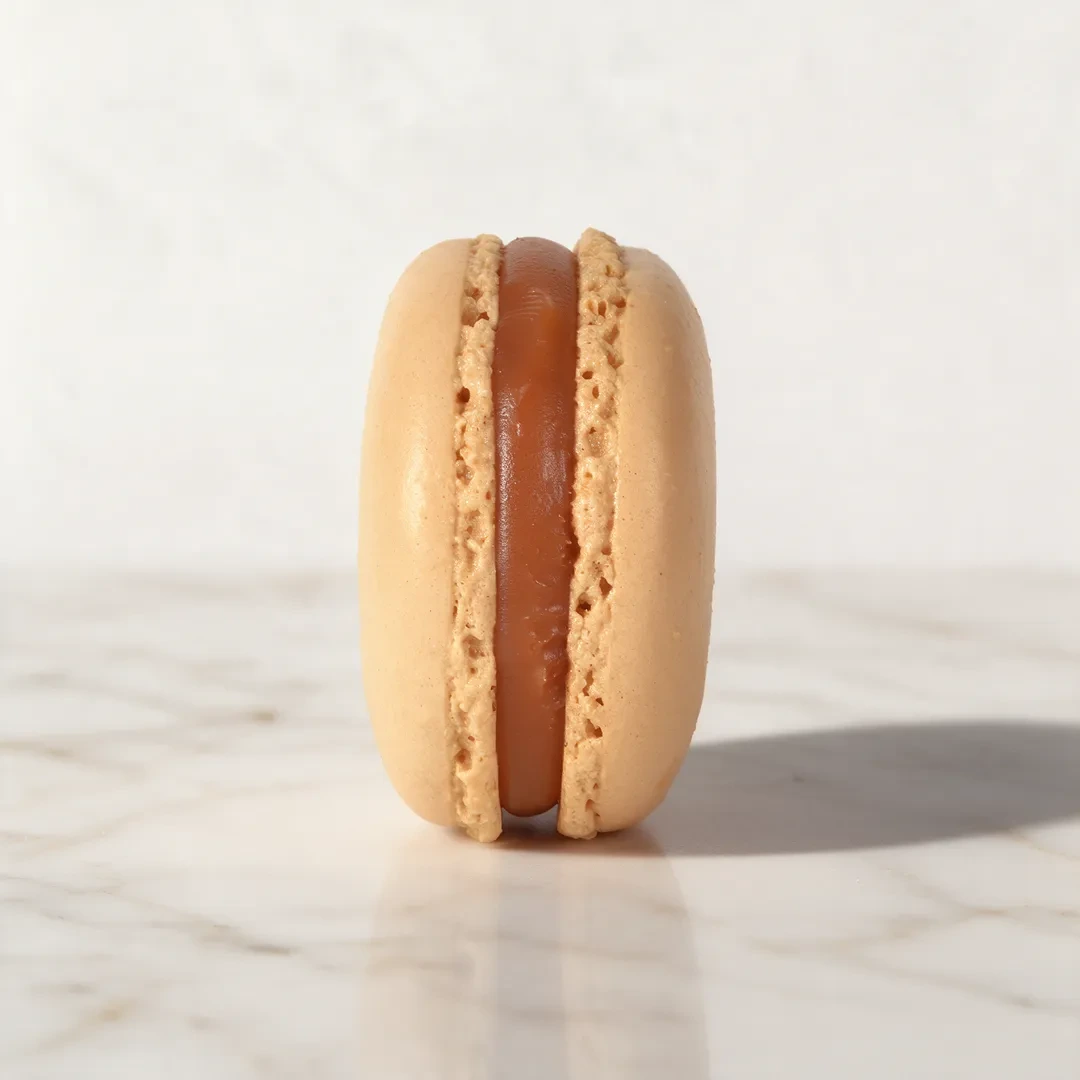 Macaron caramel à la coque beige, ganache au caramel beurre salé, posé sur marbre clair, de Stéphane Pasco, pâtissier à Nantes et Vertou